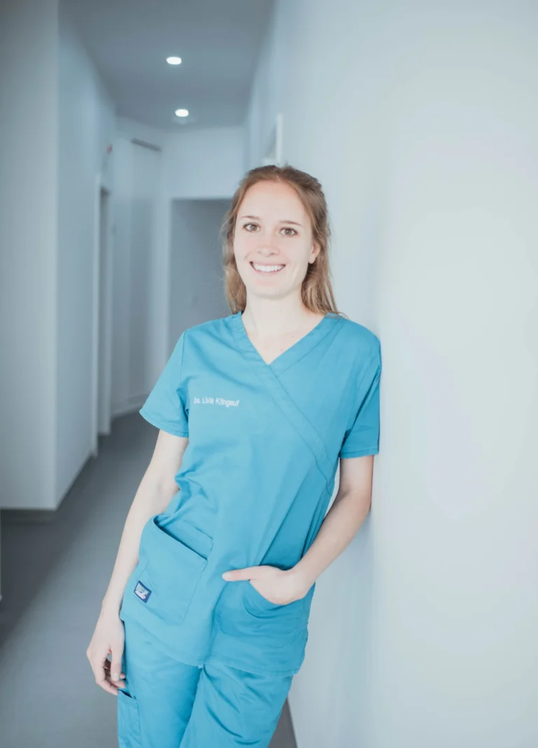 Profissional de saúde sorridente, de uniforme verde no corredor da clínica, representando cuidados médicos e bem-estar.