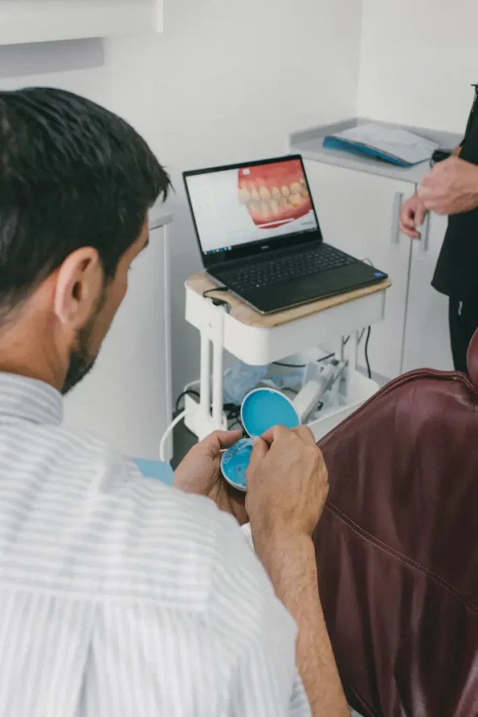 Paciente em consulta odontológica a visualizar uma imagem digital de dentes em computador, com profissional de odontologia ao lado. Ambiente clínico organizado e equipamento odontológico ao fundo.